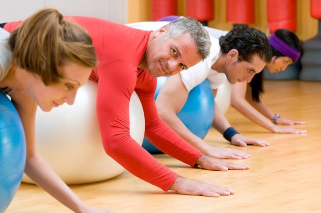 Fitness class lying on front on fitness balls at gym, mature instructor in the centre.