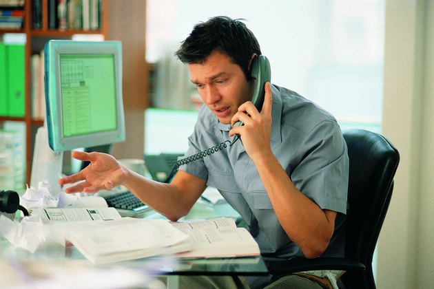 Exasperated man on phone at cluttered desk