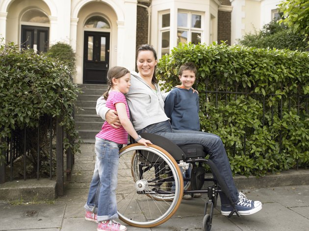 Mother in wheelchair outside house, arms around children (7-9) smiling