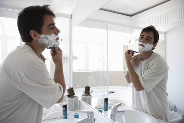 Man shaving face in bathroom mirror, side view