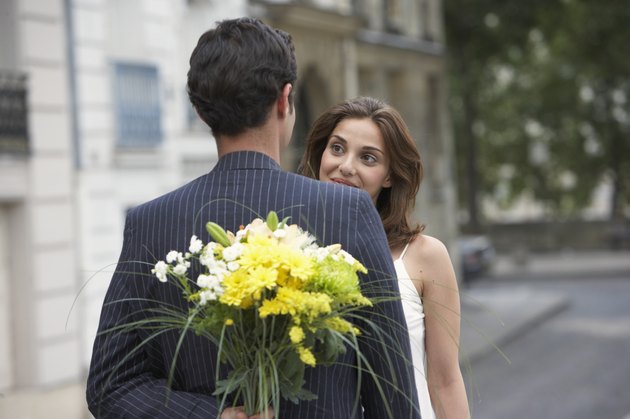 France, Paris, young couple outdoors, man holding flowers behind back