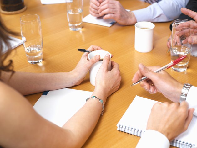 Business colleagues with drinks and notepads on table in meeting