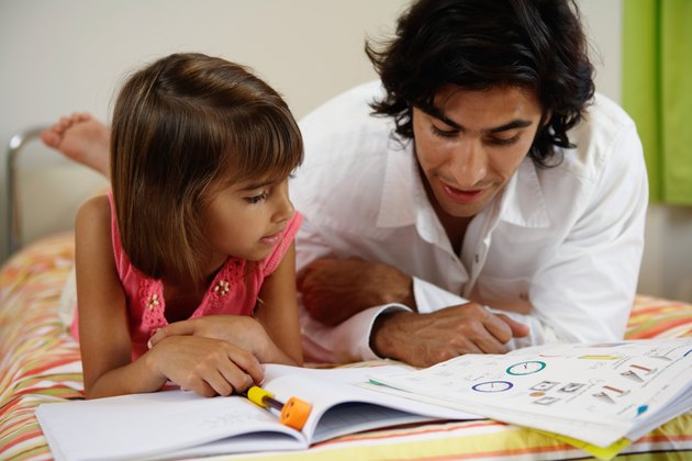 Father helping daughter (8-10) with home-work on bed