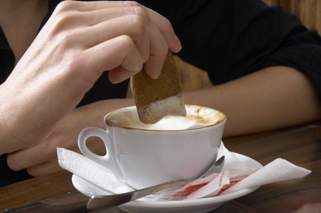 Woman dipping bisuit into coffee, close-up