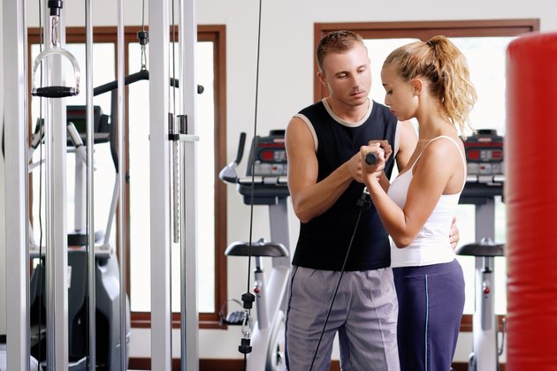 Trainer assisting woman with weight lifting apparatus