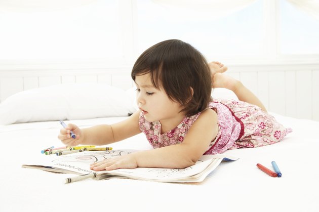 Toddler girl (21-24 months) coloring on bed, side view