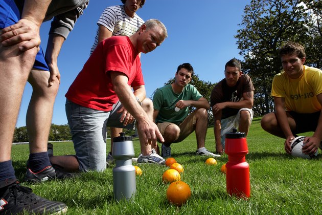 Group of men in park, planning football game by putting oranges on grass
