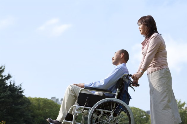 Mature couple in park, woman pushing man in wheelchair, copy space