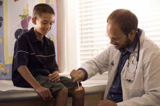 a caucasian male pediatricain checks the relexes on a young boy in his examination room