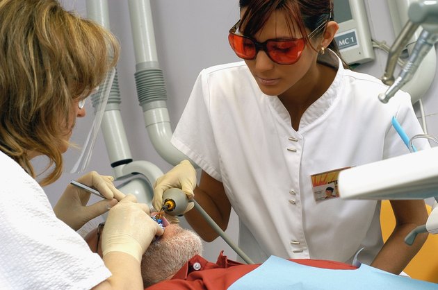 Female dentist and dental assistant working on male patient, close-up