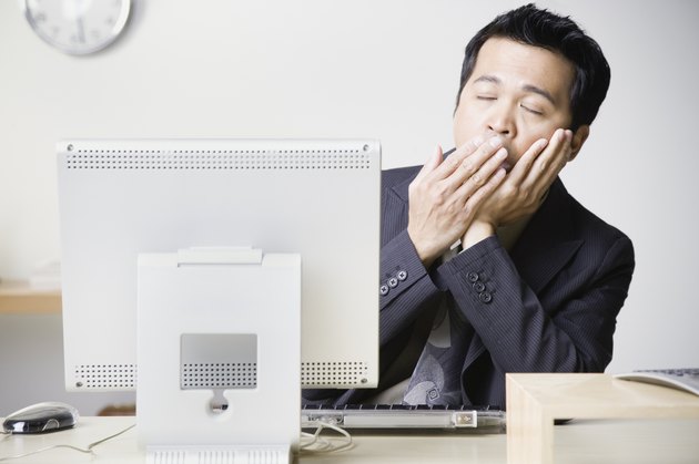 Asian businessman sitting at computer yawning