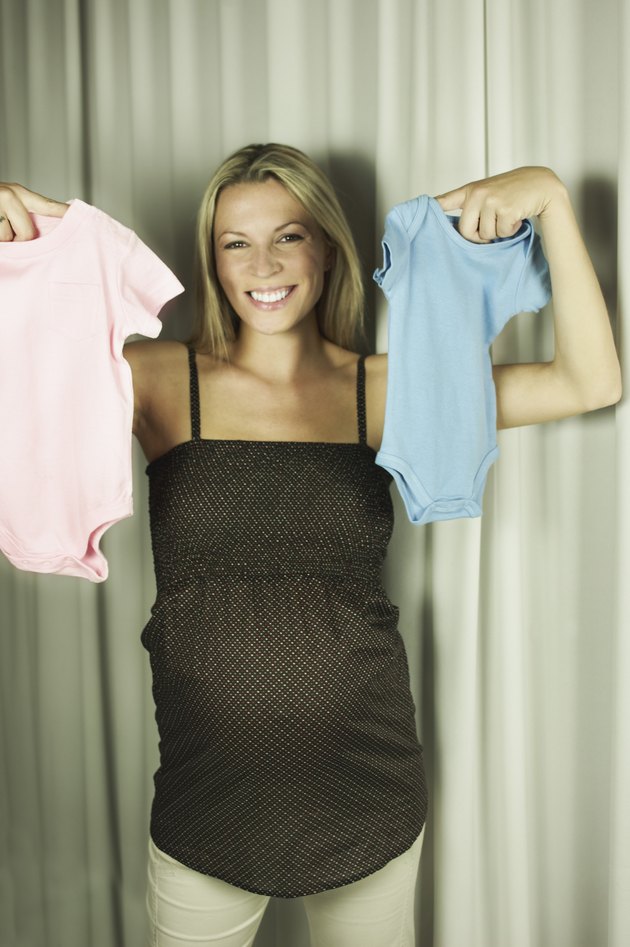Smiling pregnant woman with pink and blue onesies
