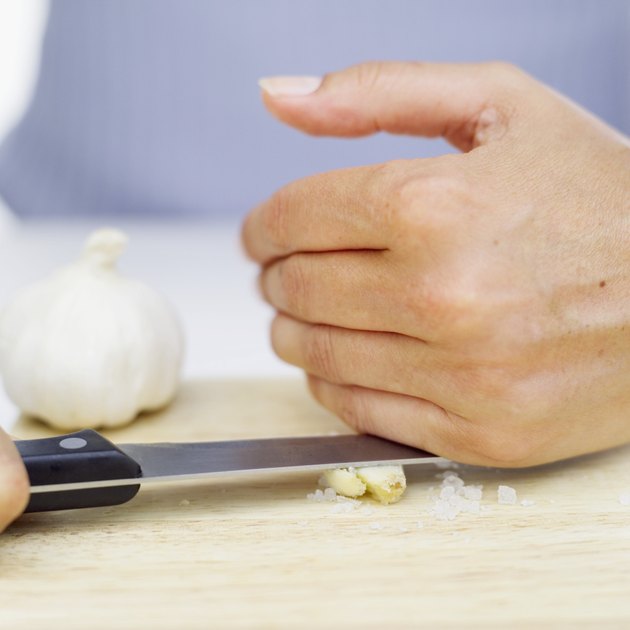 Person's hands crushing garlic with a knife