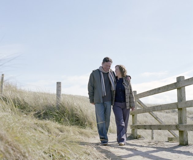 Mature couple walking on path by wooden rail, smiling