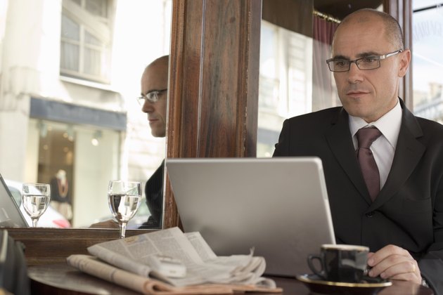 Mature businessman sitting outside cafe using laptop