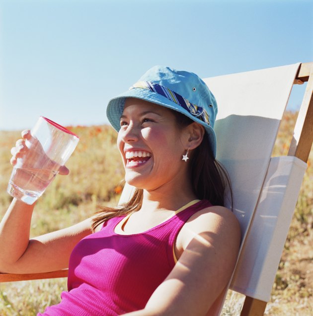 Young woman sitting in field, holding glass of water
