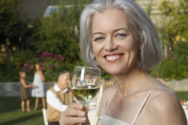 Mature woman in garden holding wine glass, smiling, portrait, close-up