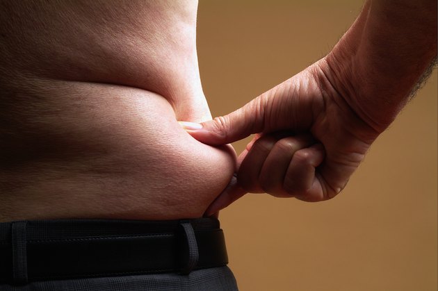 Bare-chested senior man pinching skin around waist, mid section
