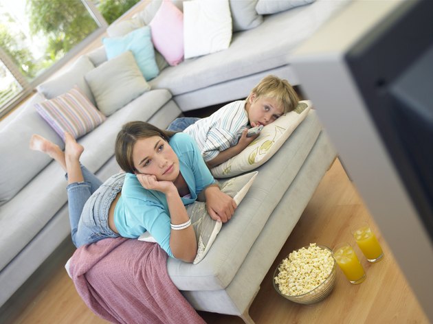 Boy (7-9) and girl (14-16) relaxing in living room watching television