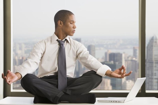 Mixed race businessman practicing yoga at desk