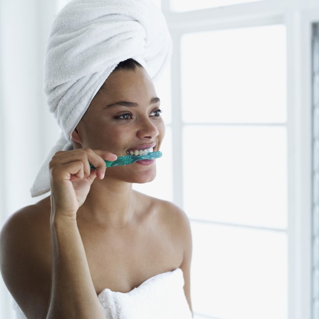 Young woman with a towel around her head brushing her teeth