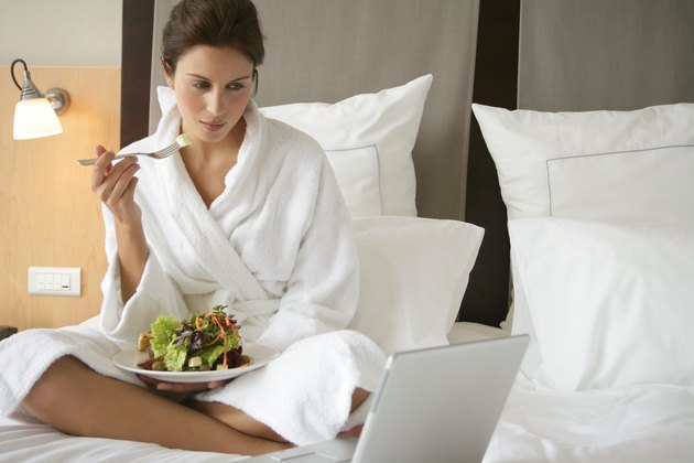 Woman wearing robe eating salad in bed with laptop