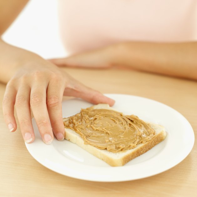 Close-up of a woman's hand holding a slice of bread with peanut butter