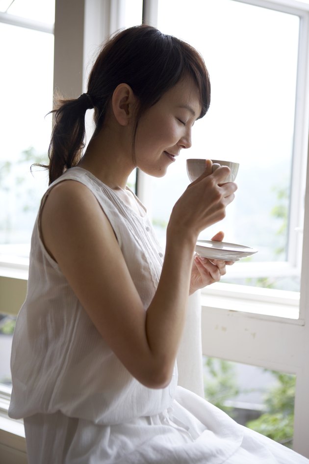 Woman drinking tea by window in home