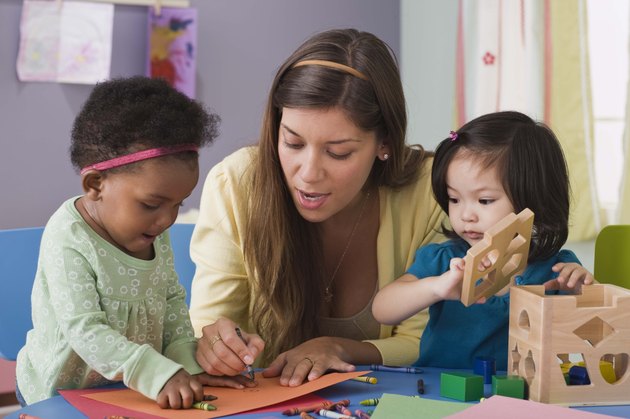 Teacher helping toddlers color at daycare