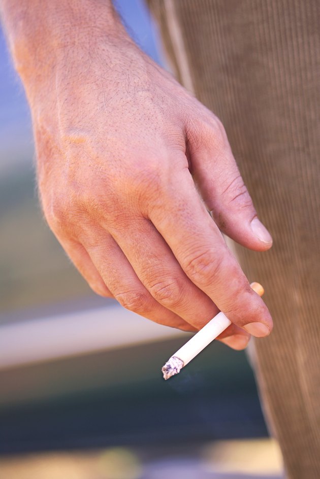 Close-up of a man's hand holding a cigarette at his side.
