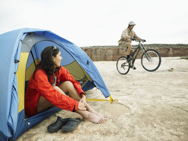Woman sitting in tent, man riding mountain bike in background