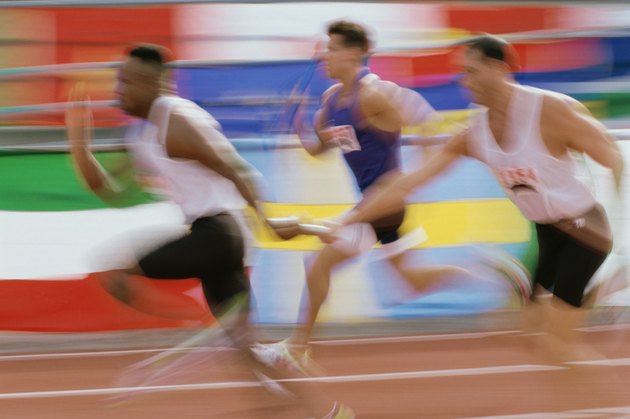 Side profile of runners exchanging baton at a relay race