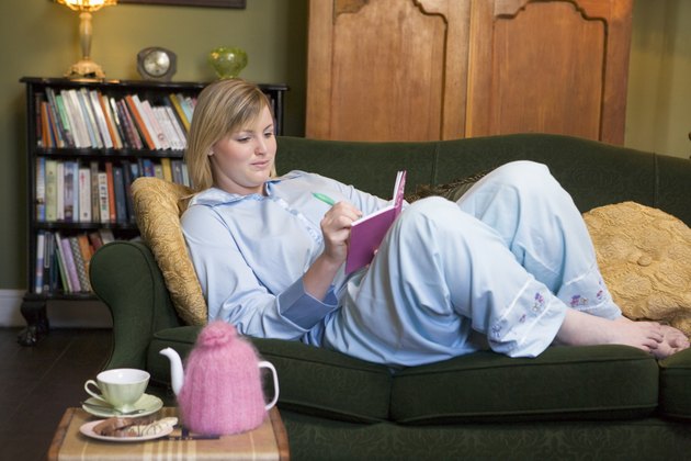 Young woman lying on sofa at home writing in her diary