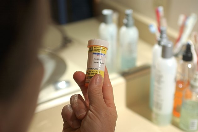 Close-up looking over a woman's shoulder to her holding a bottle of prescription medication