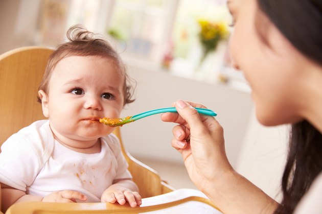 Happy Baby Being Fed In High Chair At Meal Time