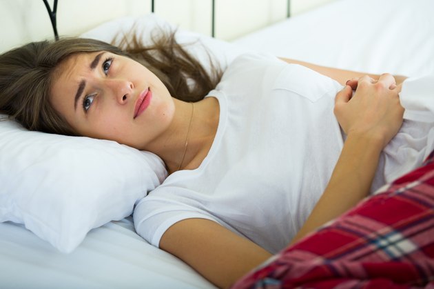 Portrait of brunette girl in bed with stomach pain