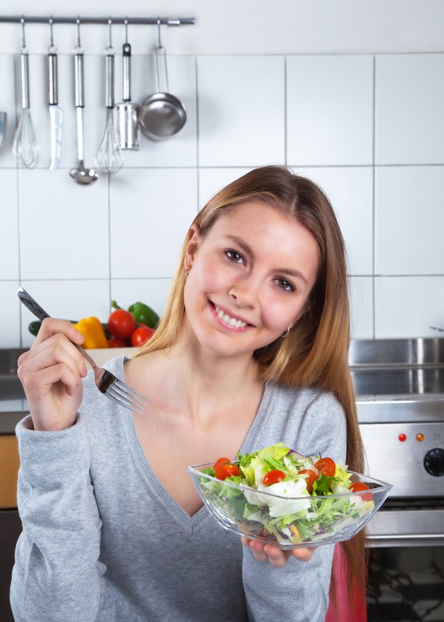 Laughing young woman at kitchen with fresh salad