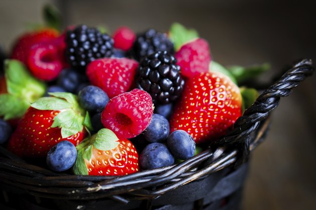 Mix of fresh berries in a basket on wooden background