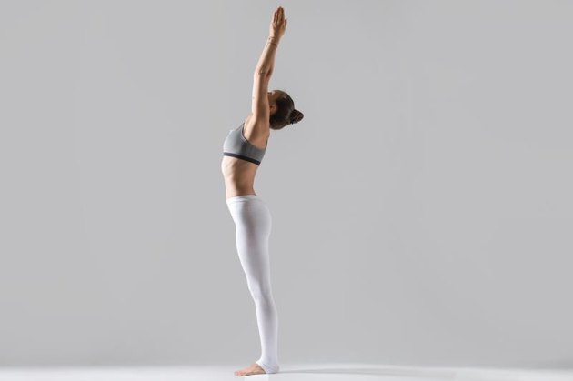 Young attractive woman practicing yoga, standing in mountain exercise, Tadasana pose, working out wearing sportswear, white pants, top, indoor full length, isolated, grey studio background