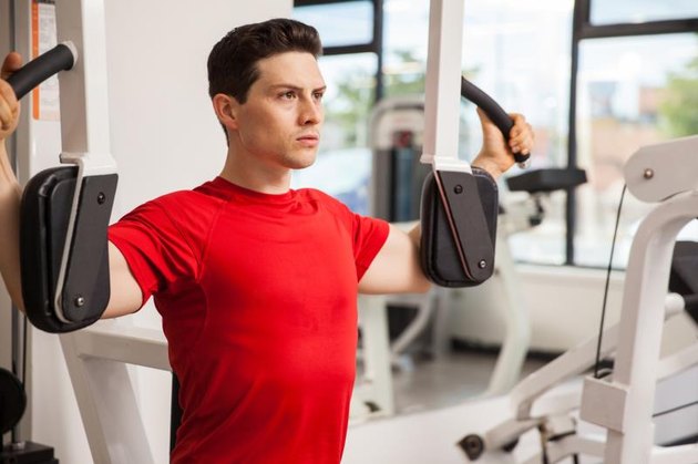 Profile view of a good looking young man exercising on a pec deck machine at a gym