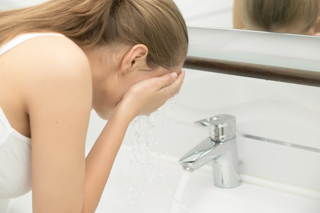 Young female washing her face tap clear water near sink