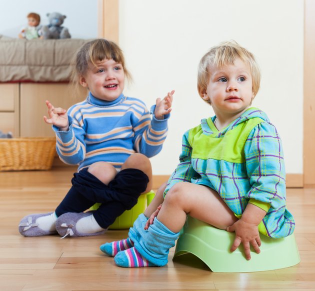 Two siblings sitting on chamber pots