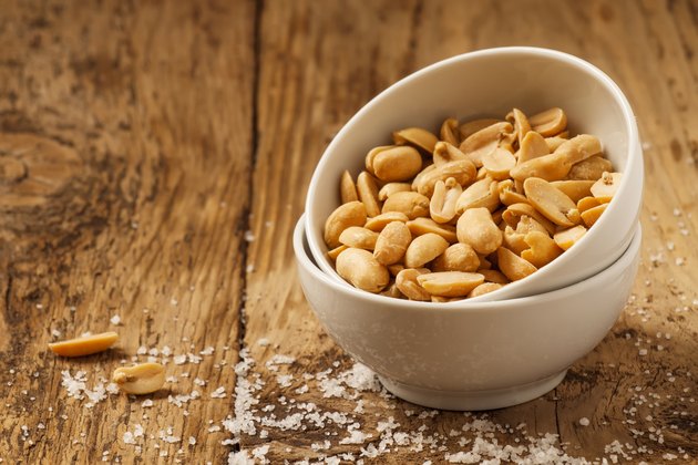 Roasted peanuts and salt in a bowl on wooden background