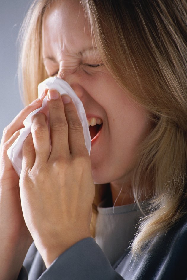Woman sneezing, holding tissue to nose