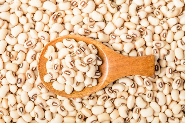 uncooked white cow pea beans in wooden spoon, top view
