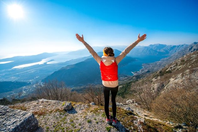 Sport woman in red vest standing on the top of mountain