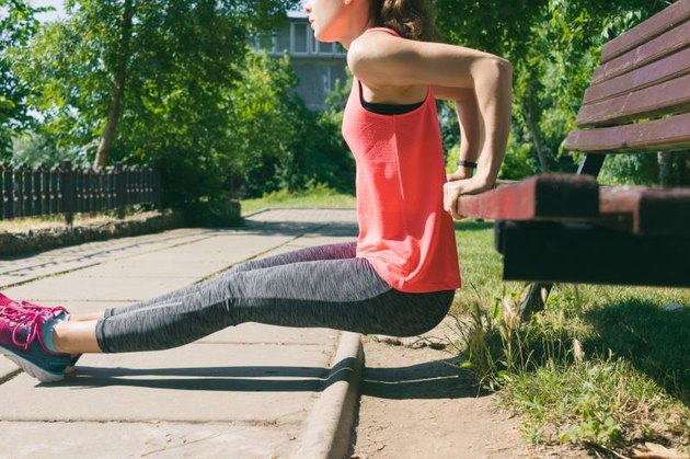 Woman in sportswear doing exercise on triceps on a park bench