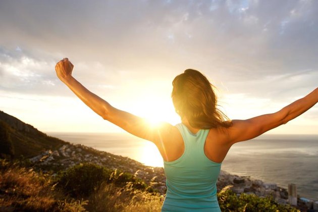 Portrait of woman from behind stretching out her arms in front of sunrise