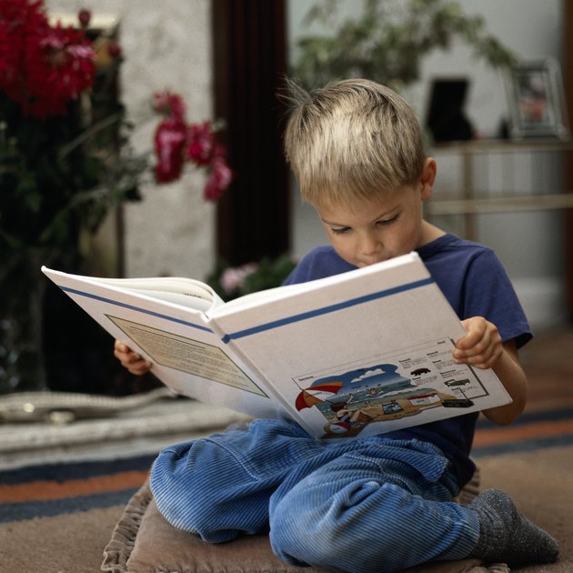 Kneeling boy reading book at home
