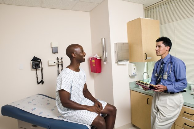 Mid adult man sitting on an examination table in a doctor's office talking to a male doctor